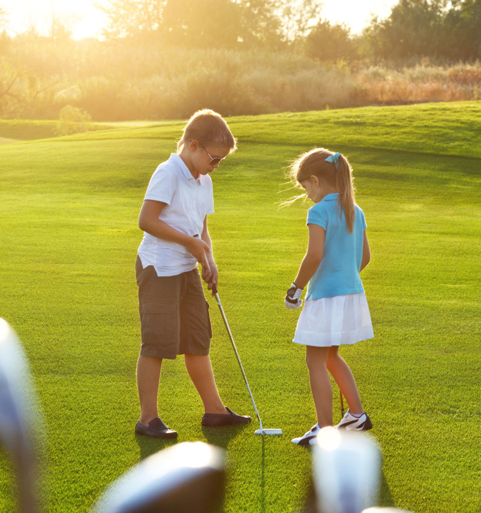 Two children playing golf on a sunny day, focusing on putting on a lush green golf course.