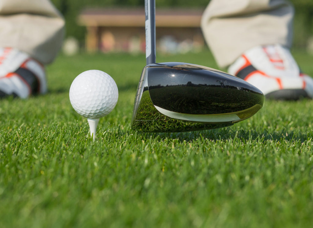 Golf club and ball on tee, ready for swing on lush green grass.