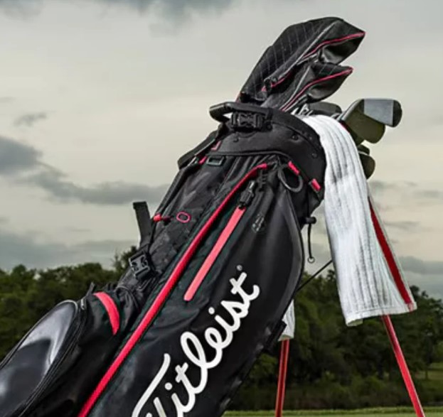 Golf bag with clubs and towel on a course, cloudy sky in background.