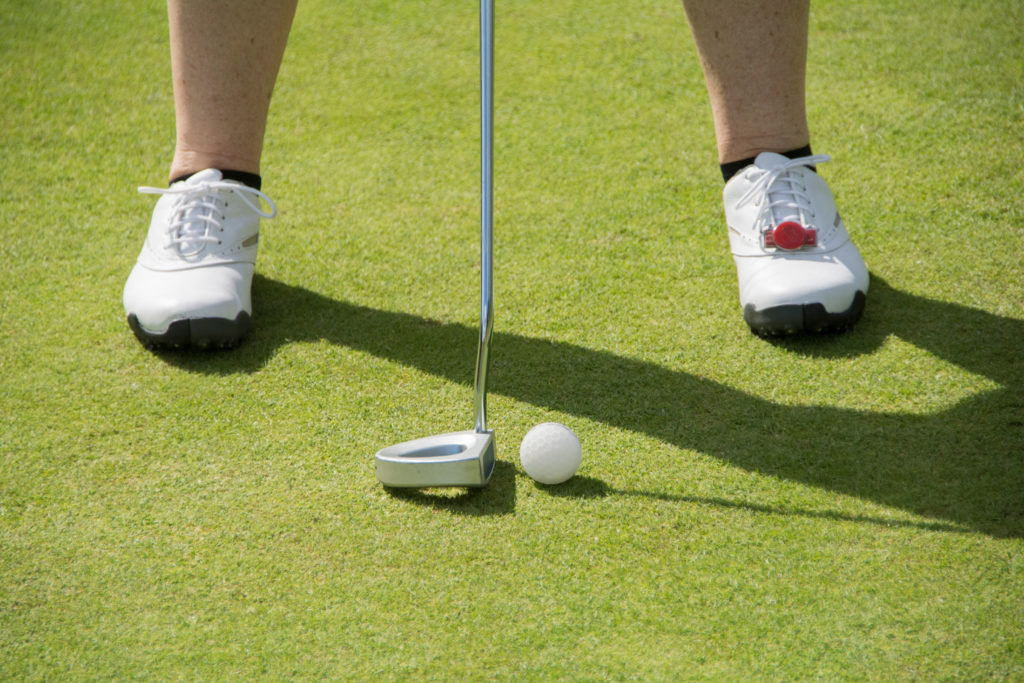 Golfer aiming putt on green with white shoes and golf ball, focusing on precision and alignment in sunny weather.