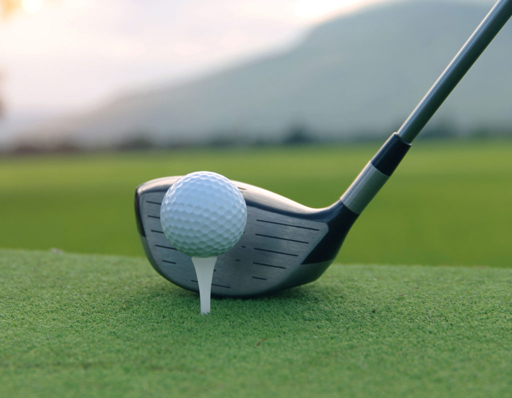 Golf ball on a tee with a driver club on a lush green fairway, ready for a perfect strike.