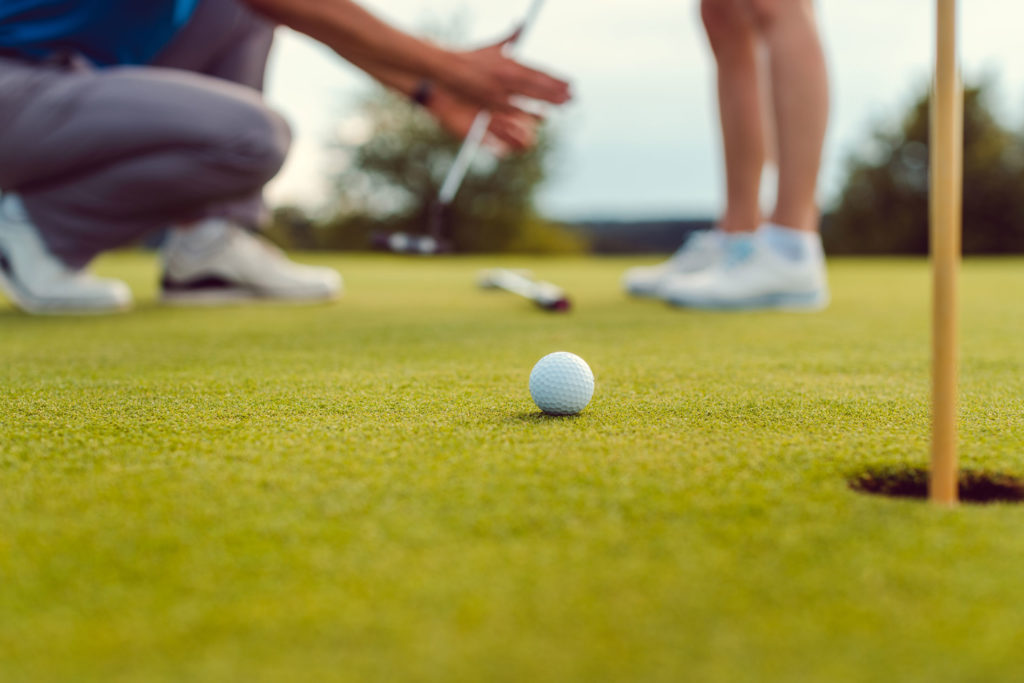 Golf ball on green near the hole, with players preparing to putt, focusing on precision and technique.