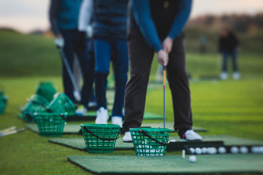 Golfer practicing swings at driving range with green ball baskets in line.