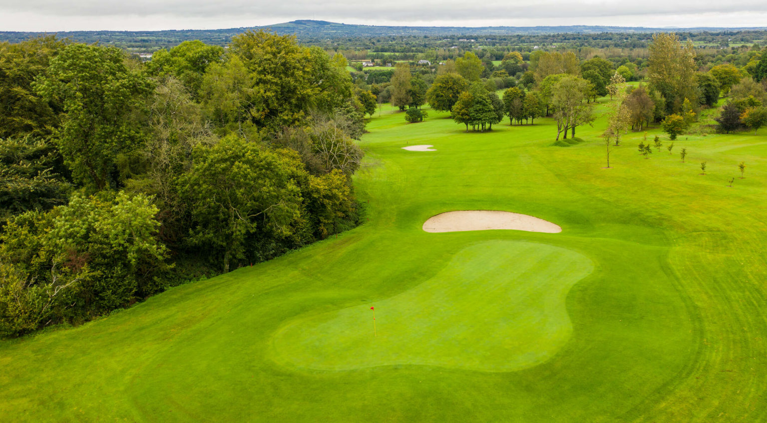 Aerial view of a lush green golf course with sand bunkers, surrounded by trees and scenic landscape.