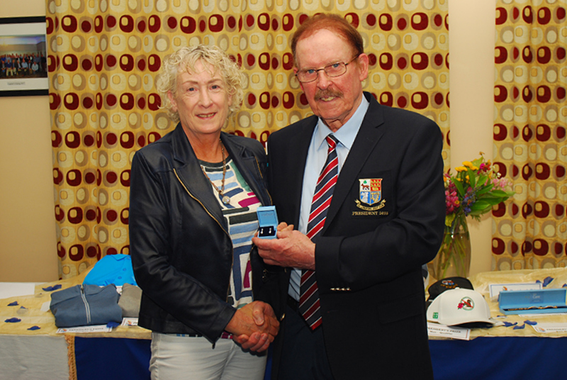 Person receiving an award from another person in a formal setting with a patterned curtain backdrop.
