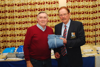 Two men in a room holding a folded blue garment, table with more garments in the background.