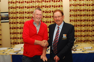 Two men shaking hands at an award ceremony, smiling and dressed in formal attire.