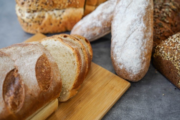 Assorted breads on a wooden board, featuring sliced loaf and rustic, seeded varieties on a gray surface.