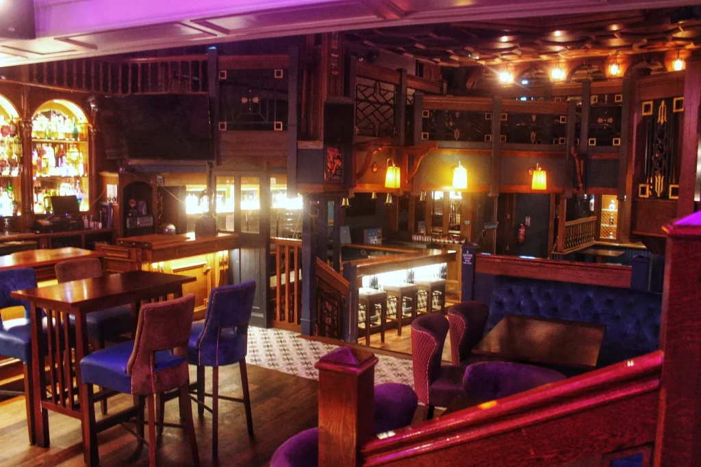 Cozy dimly-lit bar interior with wooden decor, plush seating, and glowing lamps.