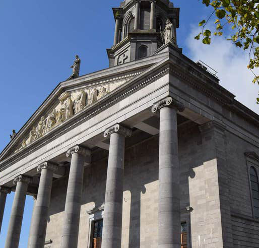 Historic stone building with columns under a blue sky, showcasing classical architecture details.