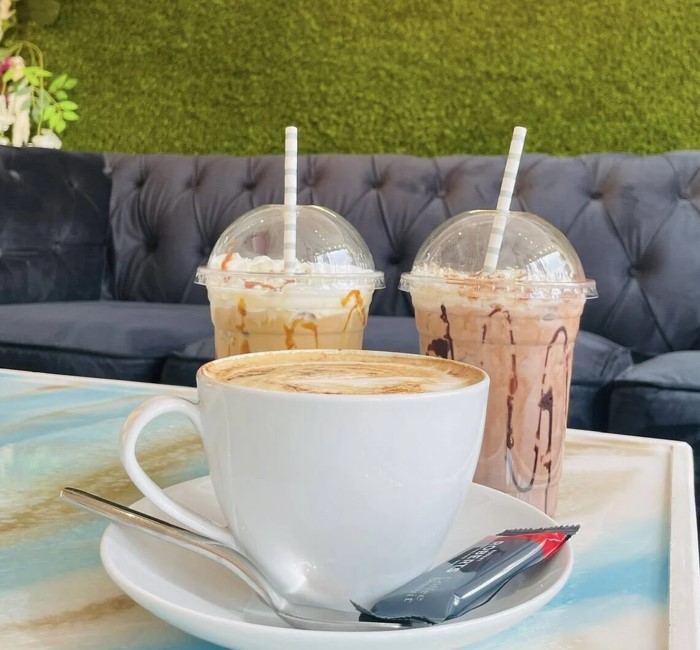 Cappuccino and two iced coffees on a table in a cozy cafe with a green wall backdrop.