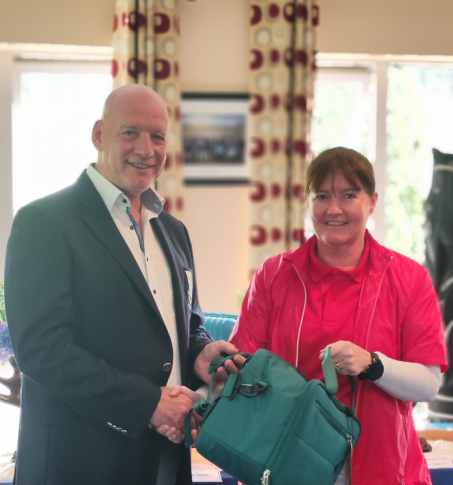 Man and woman exchanging a bag in a bright room with patterned curtains in the background.