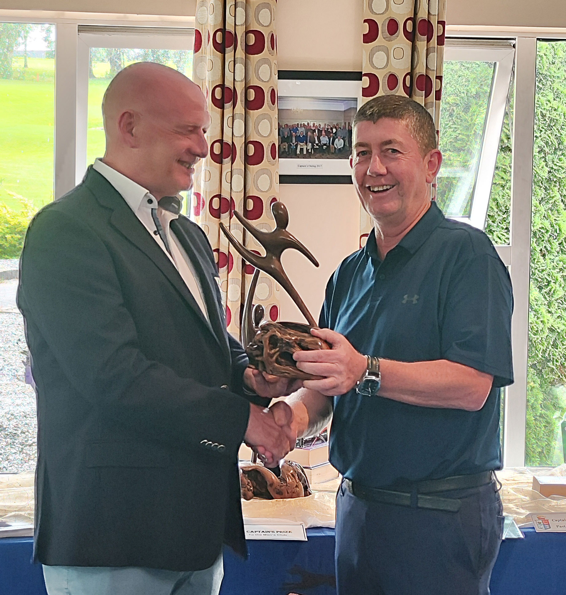 Two men shaking hands, one holding a sculpture trophy, during an indoor award ceremony.