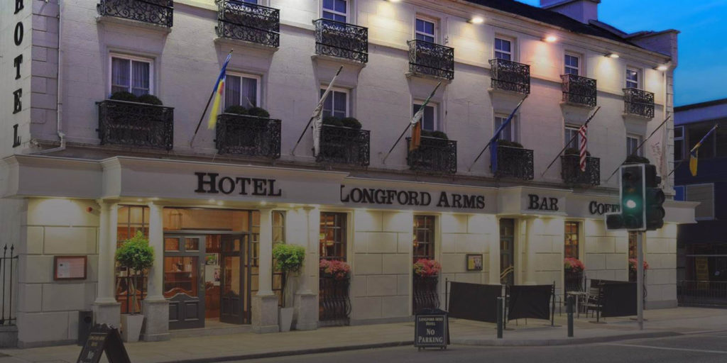 Exterior of Longford Arms Hotel at dusk with illuminated facade and hanging flags.