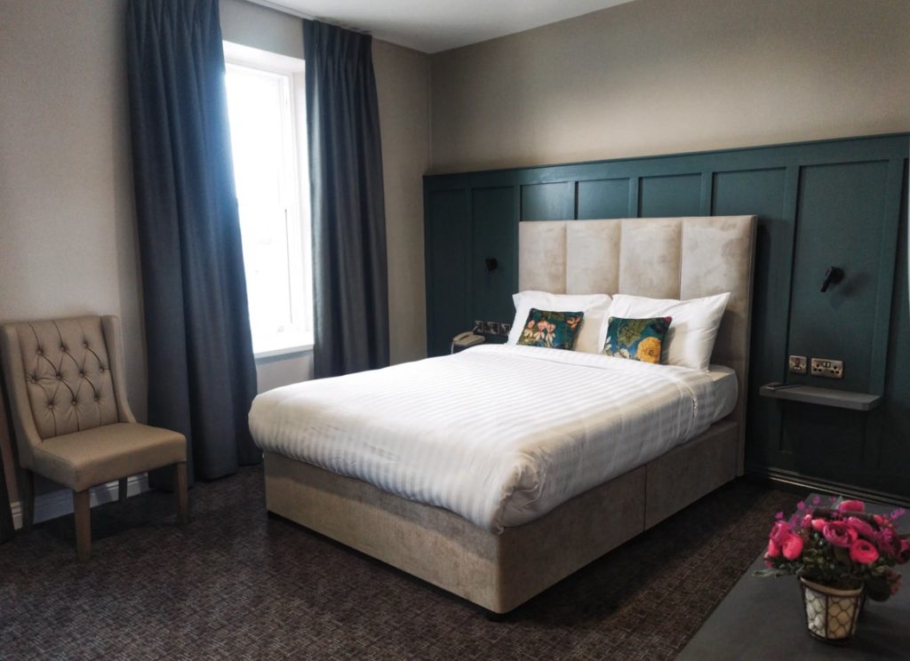 Modern hotel room with comfortable bed, tufted chair, elegant decor, and soft lighting. Perfect for a relaxing stay.