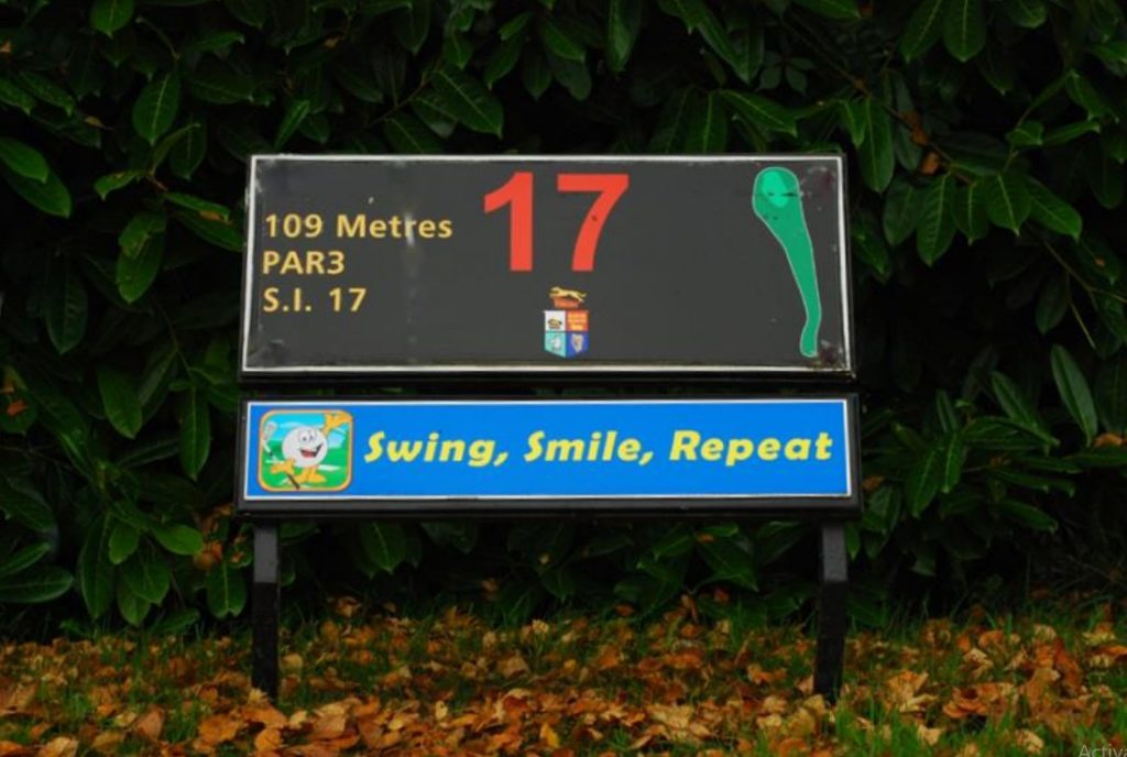 Golf hole 17 sign, par 3, 109 meters with Swing, Smile, Repeat message, surrounded by lush greenery.