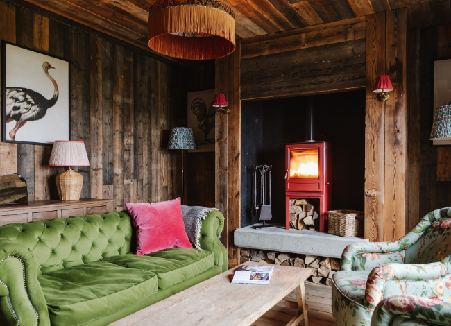 Cozy rustic living room with green sofa, wood paneling, and a lit fireplace for a warm atmosphere.