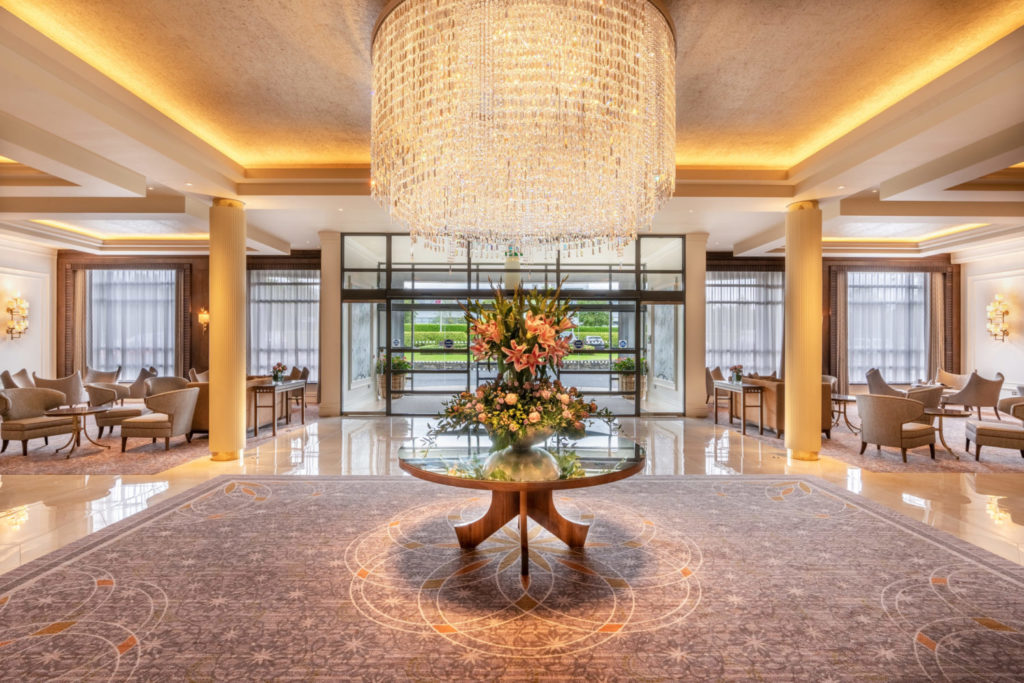 Luxurious hotel lobby with grand chandelier, elegant seating, and vibrant floral centerpiece.